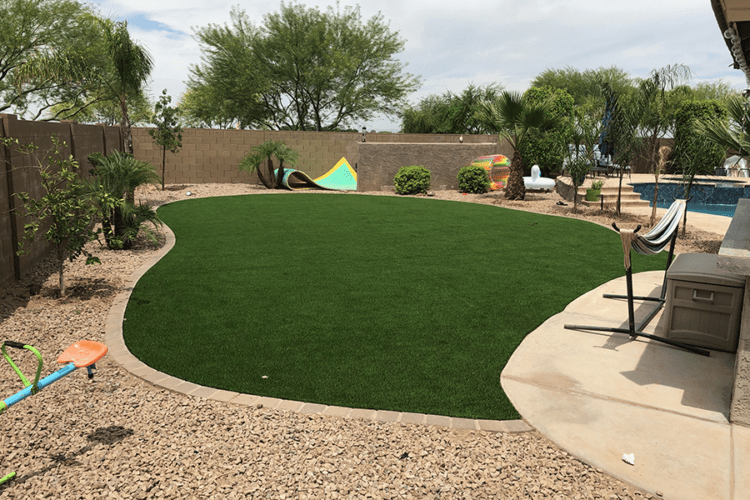 large oval artificial grass area with desert landscaping with pool toys and a hammock