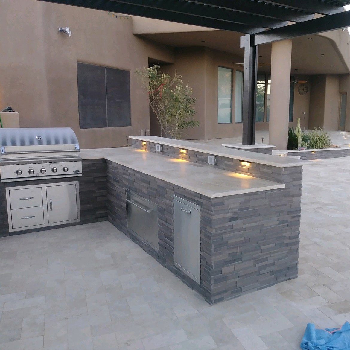 custom backyard kitchen with light pavers underneath a pergola