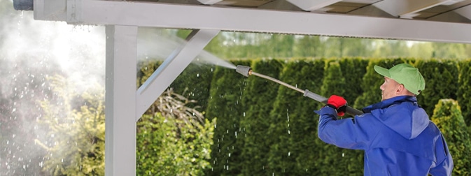 Man cleaning a pergola with a water hoze in a yard