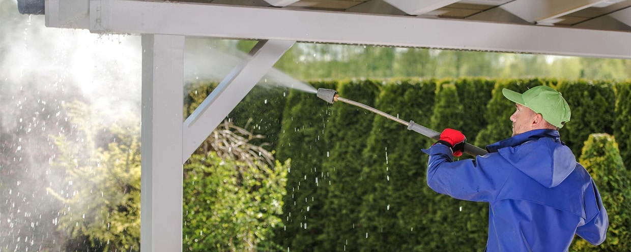 Man cleaning a white pergola with a water hose