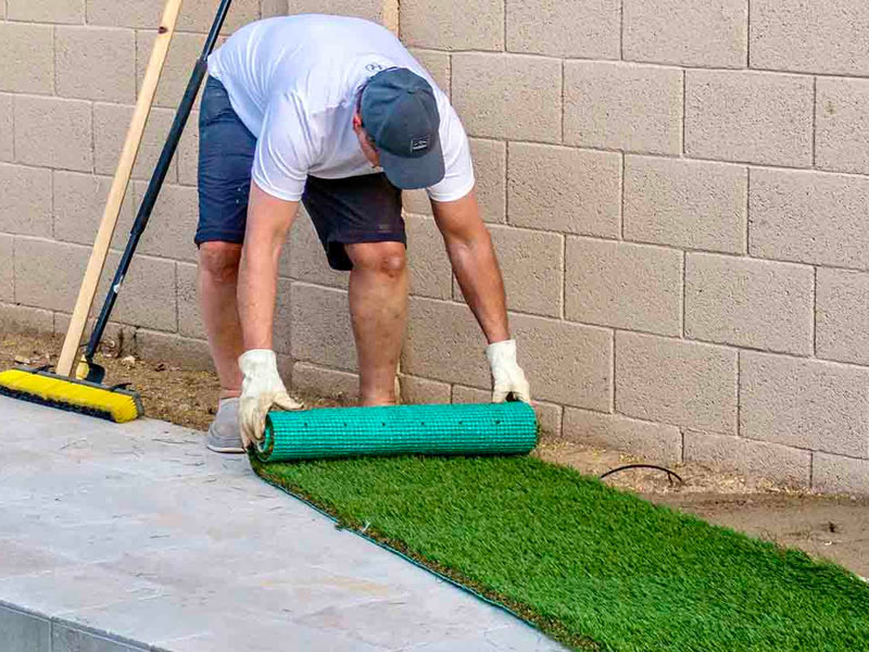 Worker rolling out roll of artificial grass during install